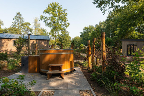 Bañera de hidromasaje de madera junto a la Tiny Loft en Veluwepark de Bosgraaf, Países Bajos, rodeada de vegetación.
