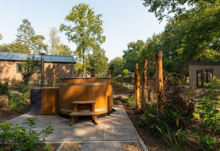 Bañera de hidromasaje de madera junto a la Tiny Loft en Veluwepark de Bosgraaf, Países Bajos, rodeada de vegetación.