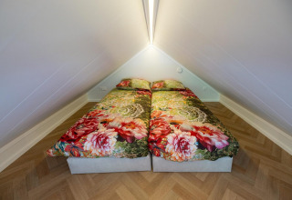 Two single beds with bright floral bedding in a cozy loft room at Tiny Loft, Veluwepark de Bosgraaf.