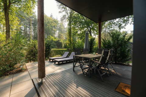 Terrasse mit Esstisch, Stühlen und Liegen bei Sand Lodge Comfort im Veluwepark de Bosgraaf, Niederlande.