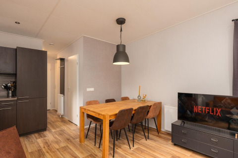 Ess- und Wohnbereich mit Holztisch und Fernseher bei Sand Lodge Comfort, Veluwepark de Bosgraaf, Niederlande.