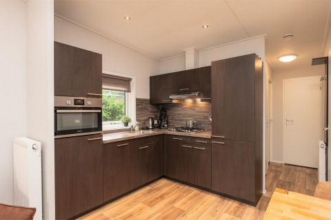 Cocina moderna en Sand Lodge Comfort, Veluwepark de Bosgraaf, Países Bajos, con gabinetes oscuros y suelo de madera.