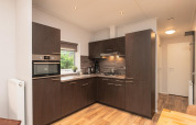 Moderne keuken in Sand Lodge Comfort, Veluwepark de Bosgraaf, Nederland, met donkere kasten en houten vloer.