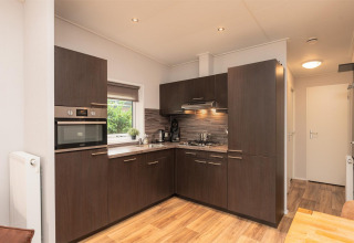 Cocina moderna en Sand Lodge Comfort, Veluwepark de Bosgraaf, Países Bajos, con gabinetes oscuros y suelo de madera.