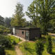 Udsigt over Heather Lodge, omgivet af frodige grønne træer og buske i et fredeligt naturområde.
