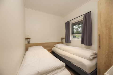 Habitación con dos camas individuales, ropa de cama blanca, ventana con cortinas grises en Heather Lodge, Veluwepark de Bosgraaf.