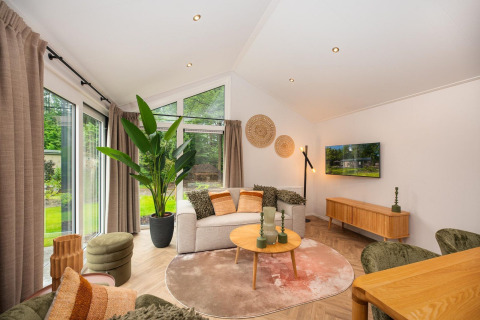 Woonkamer met moderne meubels, zetel, salontafel, grote ramen en groen uitzicht in Velthorst Comfort lodge.