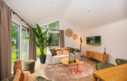 Stue med moderne indretning, sofa, stuebord, store vinduer og grøn udsigt i Velthorst Comfort lodge.