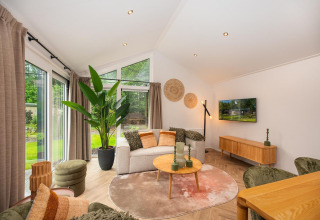 Woonkamer met moderne meubels, zetel, salontafel, grote ramen en groen uitzicht in Velthorst Comfort lodge.