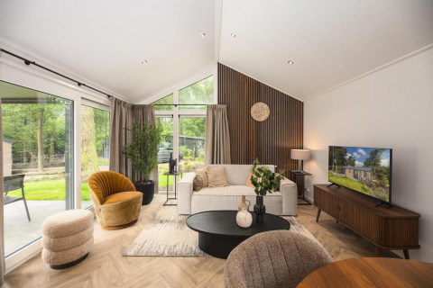 Sala moderna en la cabaña Velthorst Comfort en Veluwepark de Bosgraaf, Países Bajos, con grandes ventanales y decoración elegante.