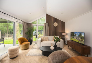 Sala moderna en la cabaña Velthorst Comfort en Veluwepark de Bosgraaf, Países Bajos, con grandes ventanales y decoración elegante.