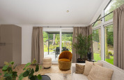 Stue i Velthorst Comfort-lodge på Veluwepark de Bosgraaf, Nederlandene, med store vinduer og moderne indretning.