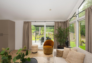 Woonkamer in Velthorst Comfort-lodge van Veluwepark de Bosgraaf, Nederland, met grote ramen en gezellige inrichting.