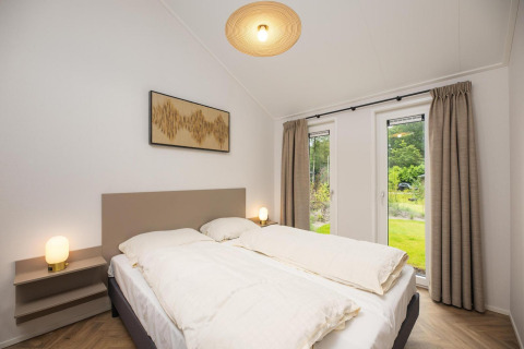 Dormitorio moderno con cama doble, grandes ventanales y cortinas en Velthorst Comfort en Veluwepark de Bosgraaf.