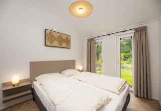 Dormitorio moderno con cama doble, grandes ventanales y cortinas en Velthorst Comfort en Veluwepark de Bosgraaf.