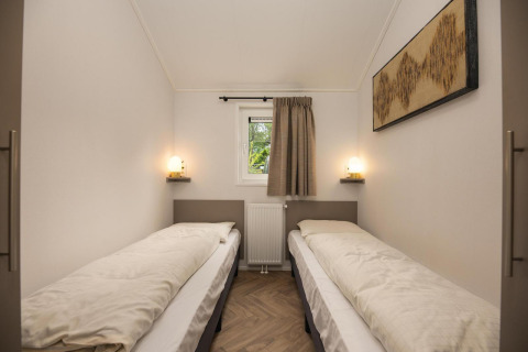 Habitación con dos camas individuales, pequeña ventana, calefacción y arte mural en Velthorst Comfort.