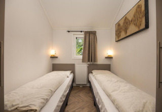 Habitación con dos camas individuales, pequeña ventana, calefacción y arte mural en Velthorst Comfort.