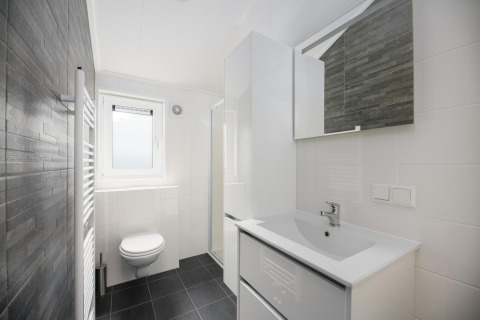 Baño moderno con inodoro suspendido, lavabo, espejo y ventana en Velthorst Comfort en los Países Bajos.