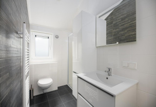 Moderne badkamer met hangtoilet, wastafel, spiegel en raam in Velthorst Comfort in Nederland.