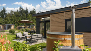 Outdoor view of Cannenburch Deluxe lodge with hot tub, stylish patio furniture, and lush green surroundings.