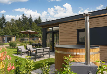 Udendørsområde ved Cannenburch Deluxe lodge med boblebad, moderne siddepladser og grøn have.