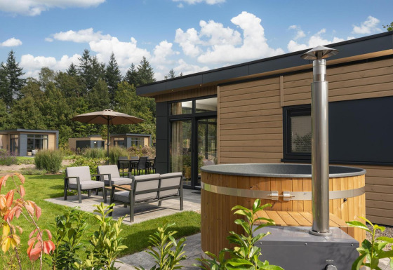 Exterior de lodge Cannenburch Deluxe con jacuzzi, muebles de terraza modernos y rodeado de vegetación.