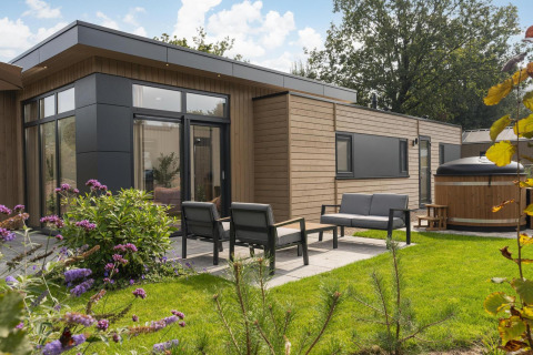 Zona exterior de la Cannenburch Deluxe lodge con muebles de jardín y jacuzzi en Veluwepark de Bosgraaf.