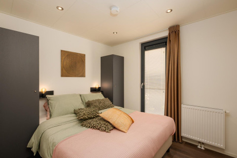 Dormitorio en Cannenburch Deluxe lodge con cama doble, decoración moderna y armarios en Veluwepark de Bosgraaf.
