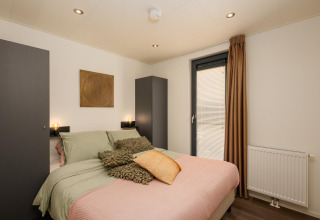 Dormitorio en Cannenburch Deluxe lodge con cama doble, decoración moderna y armarios en Veluwepark de Bosgraaf.