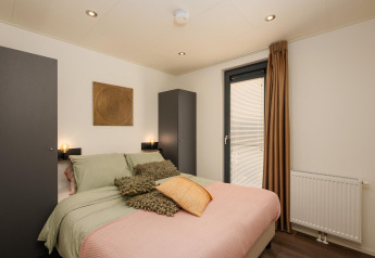Soveværelse i Cannenburch Deluxe lodge med dobbeltseng, moderne indretning og store skabe ved Veluwepark de Bosgraaf.