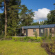 Et moderne lodgehus omgivet af grønne træer og en velplejet græsplæne under en blå himmel.