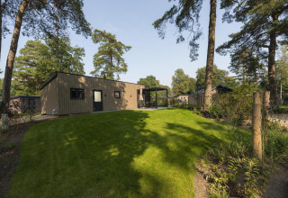 Foto einer modernen Lodge mit Rasen und Bäumen, idyllisch gelegen in einem ruhigen Waldgebiet.