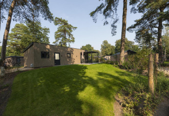 Foto af en moderne lodge omgivet af grønne græsplæner og høje træer i et fredeligt skovområde.