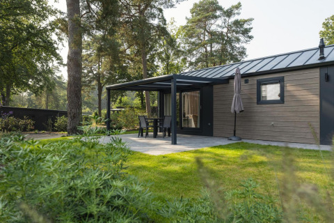 Modernes Ferienhaus mit überdachter Terrasse, Gartenmöbeln und Sonnenschirm im Grünen gelegen.