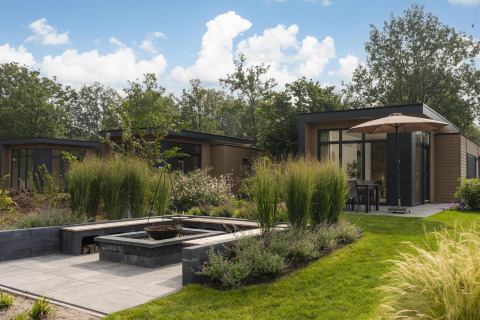 Foto exterior de un lodge moderno con jardín exuberante, muebles de terraza y sombrilla grande.