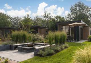Foto exterior de un lodge moderno con jardín exuberante, muebles de terraza y sombrilla grande.
