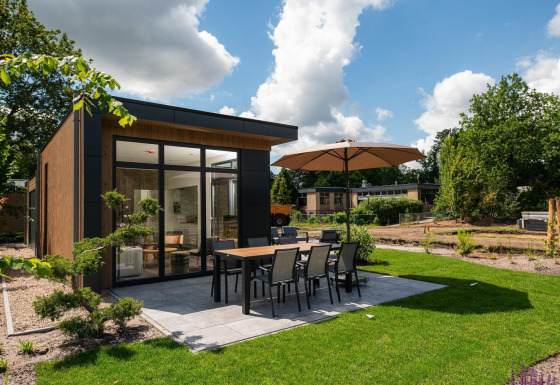 Lodge Cannenburch con patio moderno, mesa para comer, sombrilla y césped bien cuidado en un entorno natural.