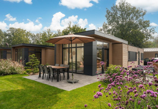 Moderna cabaña con terraza, sombrilla y mesa en jardín verde en Veluwepark de Bosgraaf, Países Bajos.
