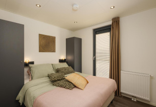 Dormitorio moderno con cama doble, dos armarios y ventana en Cannenburch Lodge, Veluwepark de Bosgraaf, Países Bajos.