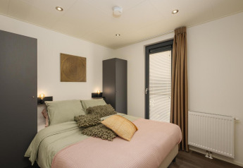 Soveværelse med moderne indretning, dobbeltseng, to skabe og vindue på Cannenburch Lodge, Veluwepark de Bosgraaf.