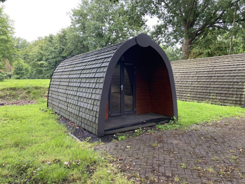 Una cabaña con techo de tejas en el césped de Het Amsterdamse Bos, Países Bajos, rodeada de árboles.