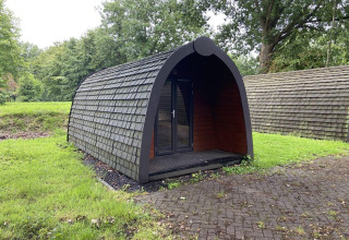 Un pod con tetto a scandole sul prato verde a Het Amsterdamse Bos nei Paesi Bassi, vicino agli alberi.