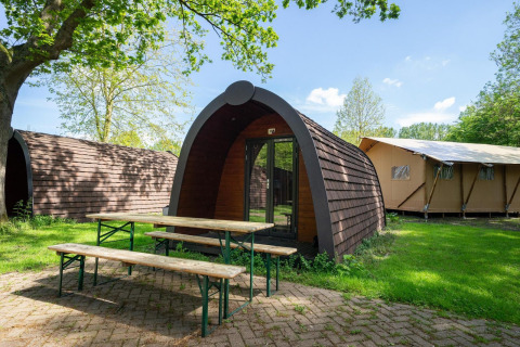 Pod en Het Amsterdamse Bos, Países Bajos, rodeado de árboles y bancos de madera sobre césped verde.