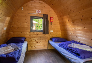 Vista interna di un pod in legno con due letti singoli e biancheria blu, presso Het Amsterdamse Bos.