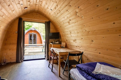 Vista interior de una cápsula de madera en Het Amsterdamse Bos, Países Bajos, con mesa, sillas y vista exterior.