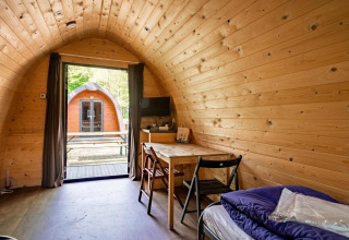 Vista interna di una pod in legno a Het Amsterdamse Bos, Paesi Bassi, con tavolo, sedie e vista sull’esterno.