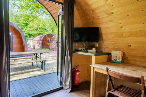 Interior de un pod de madera en Het Amsterdamse Bos, Países Bajos, con escritorio, TV y terraza exterior.