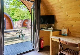Interno di una pod in legno a Het Amsterdamse Bos, Paesi Bassi, con scrivania, TV e vista su terrazza.