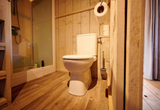 Baño moderno de madera con inodoro y ducha en una Villatent Cottage en el parque Ackersate.