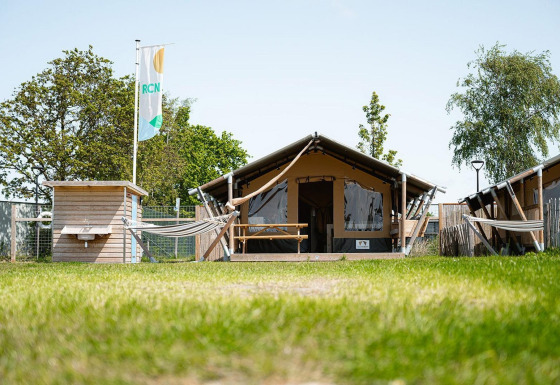 Safaritent Villatent Compact met eigen sanitair, hangmat en picknickbankje in groene omgeving.